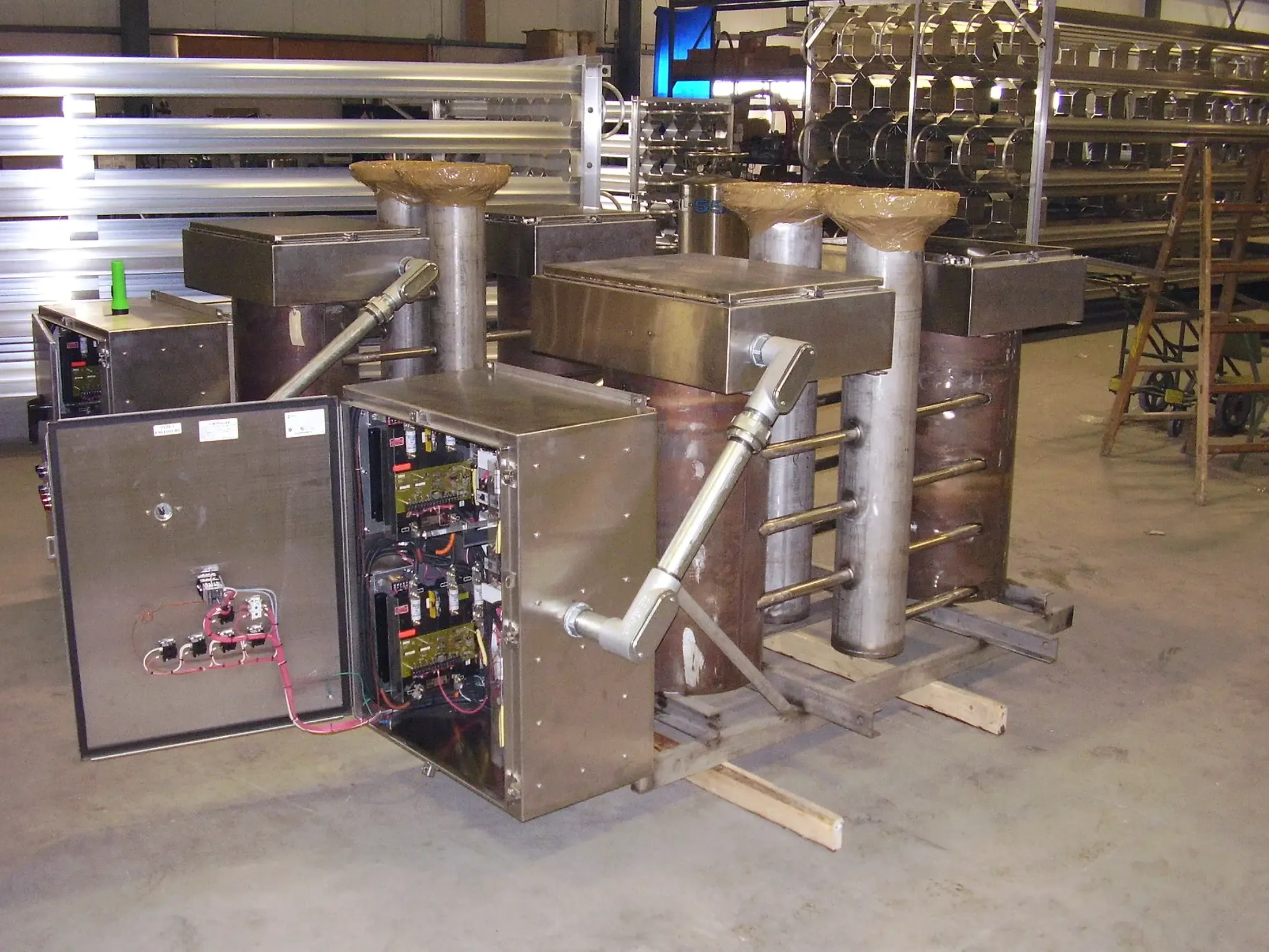 A stainless process skid at FWM with completed process piping and an opened, wired control panel during multi-process assembly