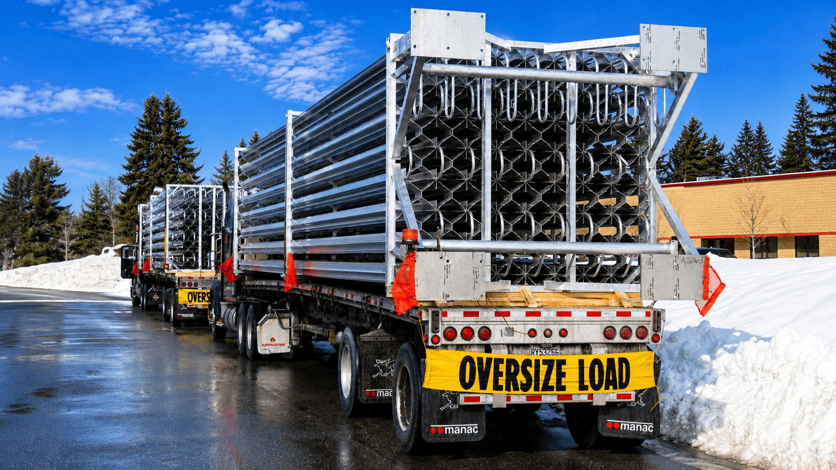 Two flatbed trucks with OVERSIZE LOAD banners hauling large galvanized FWM vaporizer arrays out for delivery