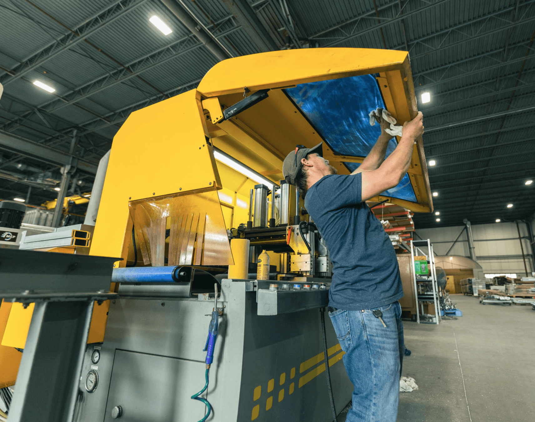 An FWM operator cleaning the safety guard of an MEP CNC cutting saw on the shop floor
