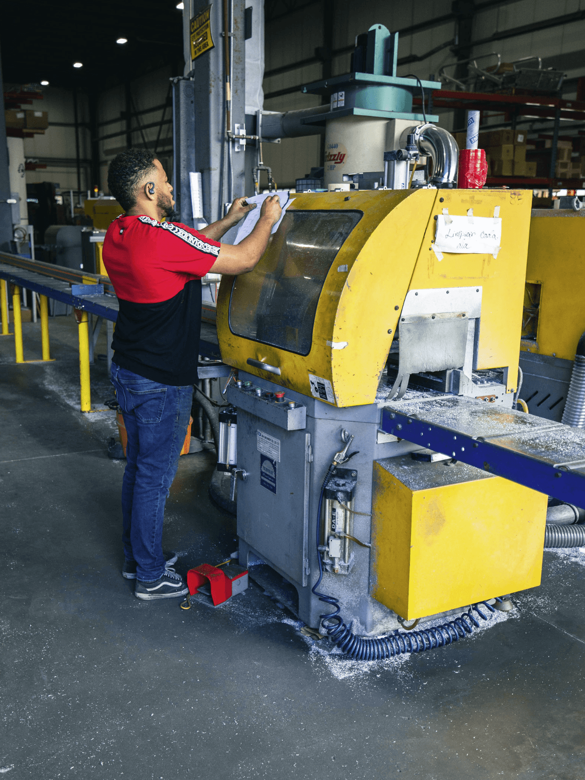 An FWM operator reviewing a work order at a cut-off saw with aluminum chips on the floor