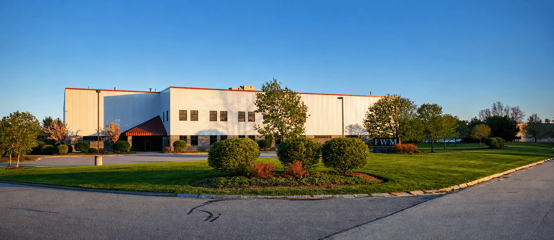 Street-level view of the FWM Inc. manufacturing headquarters in Hudson, New Hampshire, with the FWM monument sign and landscaped grounds at golden hour