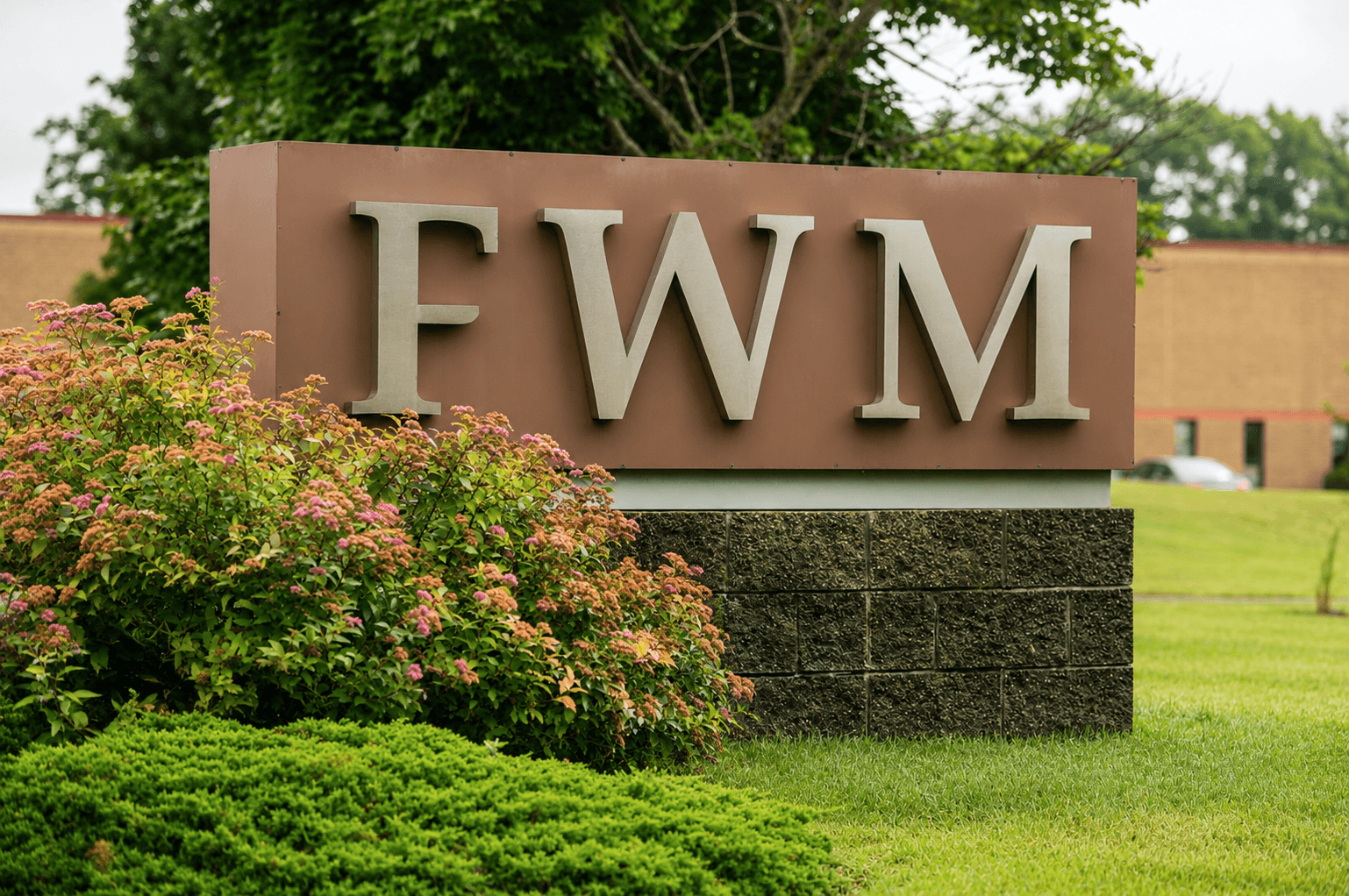 The FWM monument sign with brushed-metal lettering on a stone base at the entrance to the company's Hudson, New Hampshire facility.