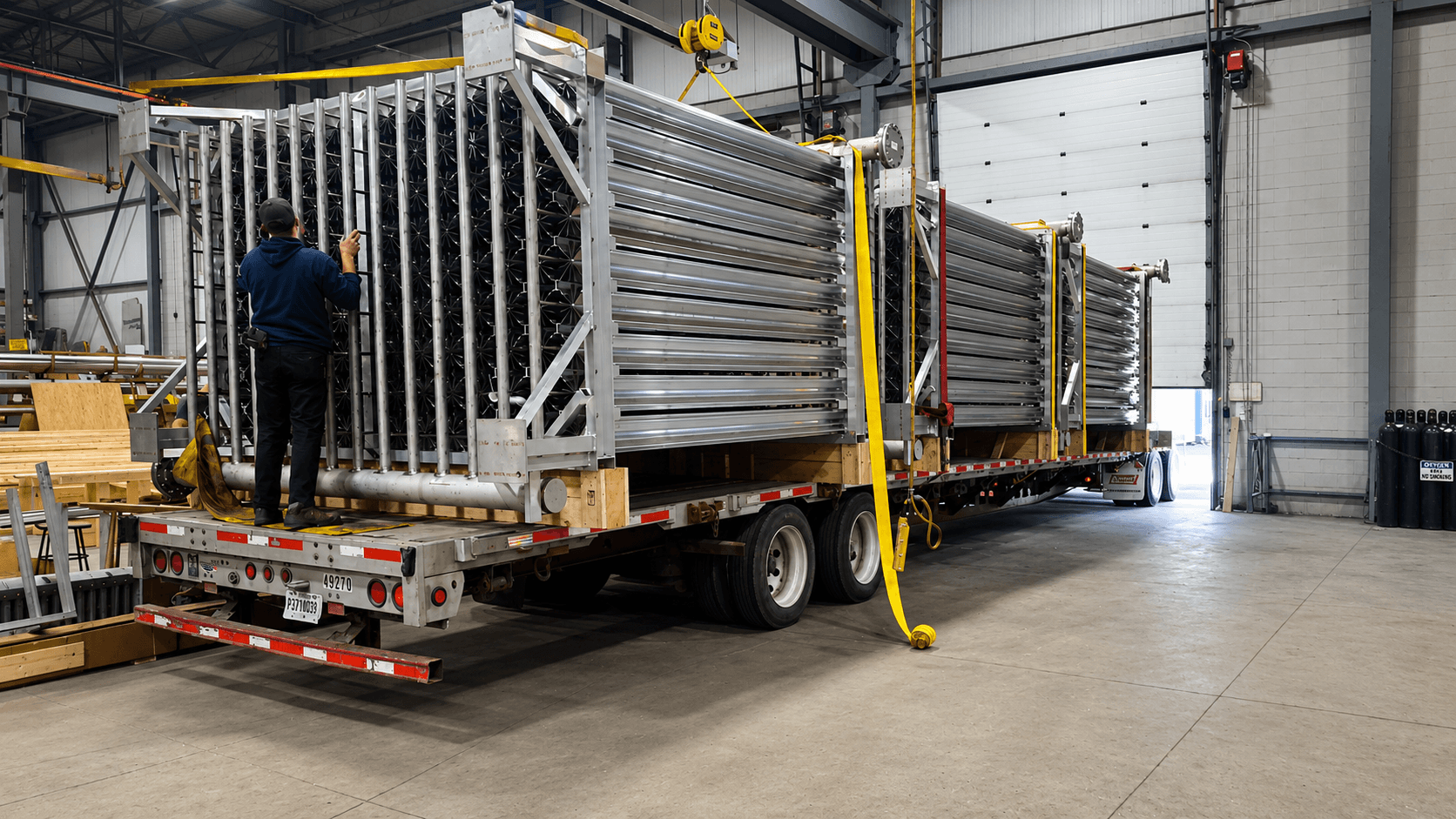 An FWM technician strapping down large finned-aluminum vaporizer arrays loaded on a flatbed trailer inside the FWM facility