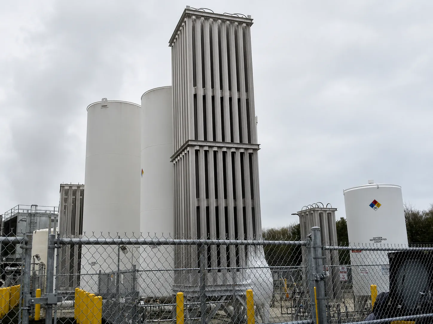 Tall FWM finned-aluminum vaporizer towers installed beside white LOX storage tanks behind a fence