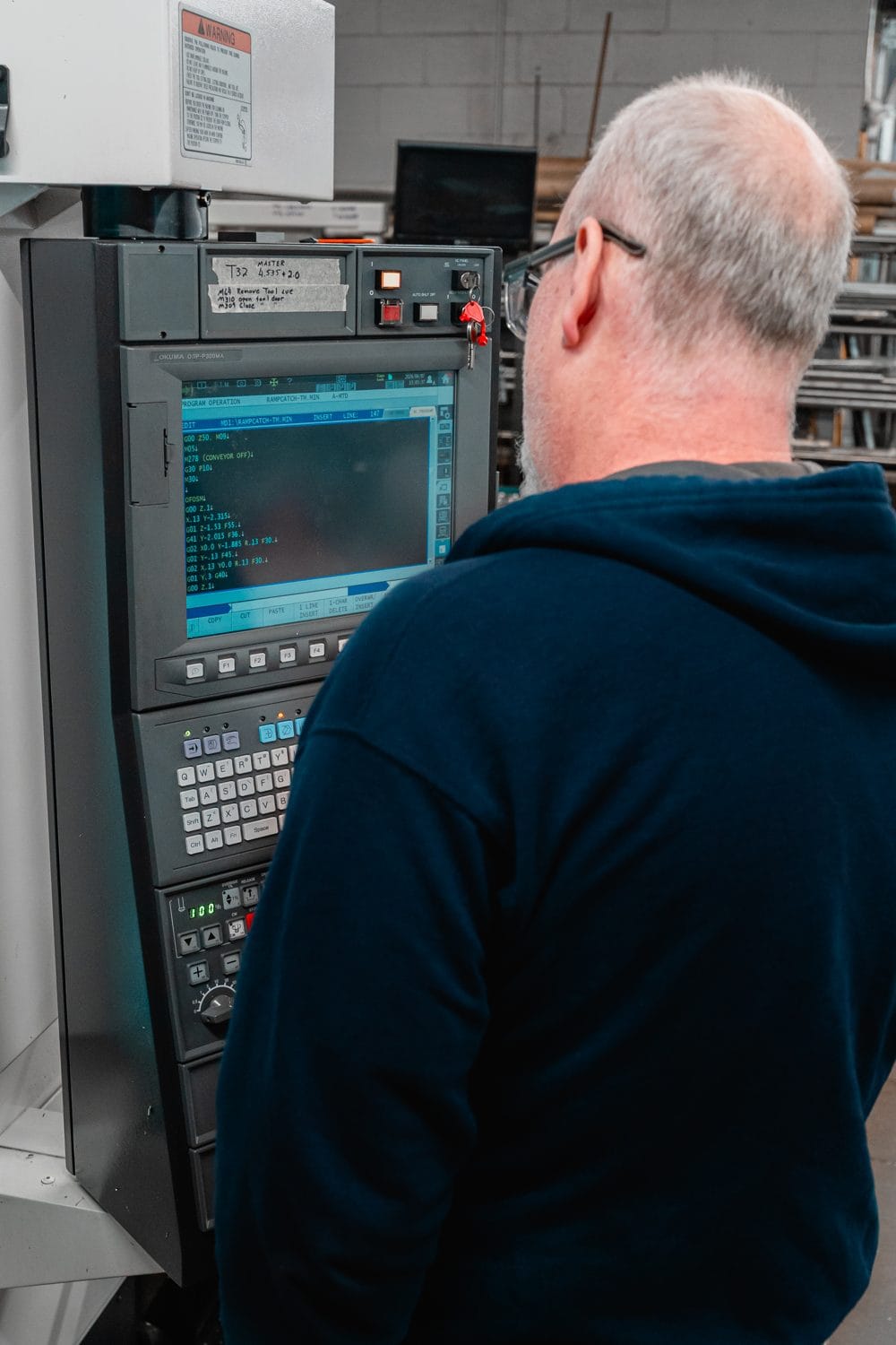 An FWM machinist at the CNC control pendant verifying a program during a production run
