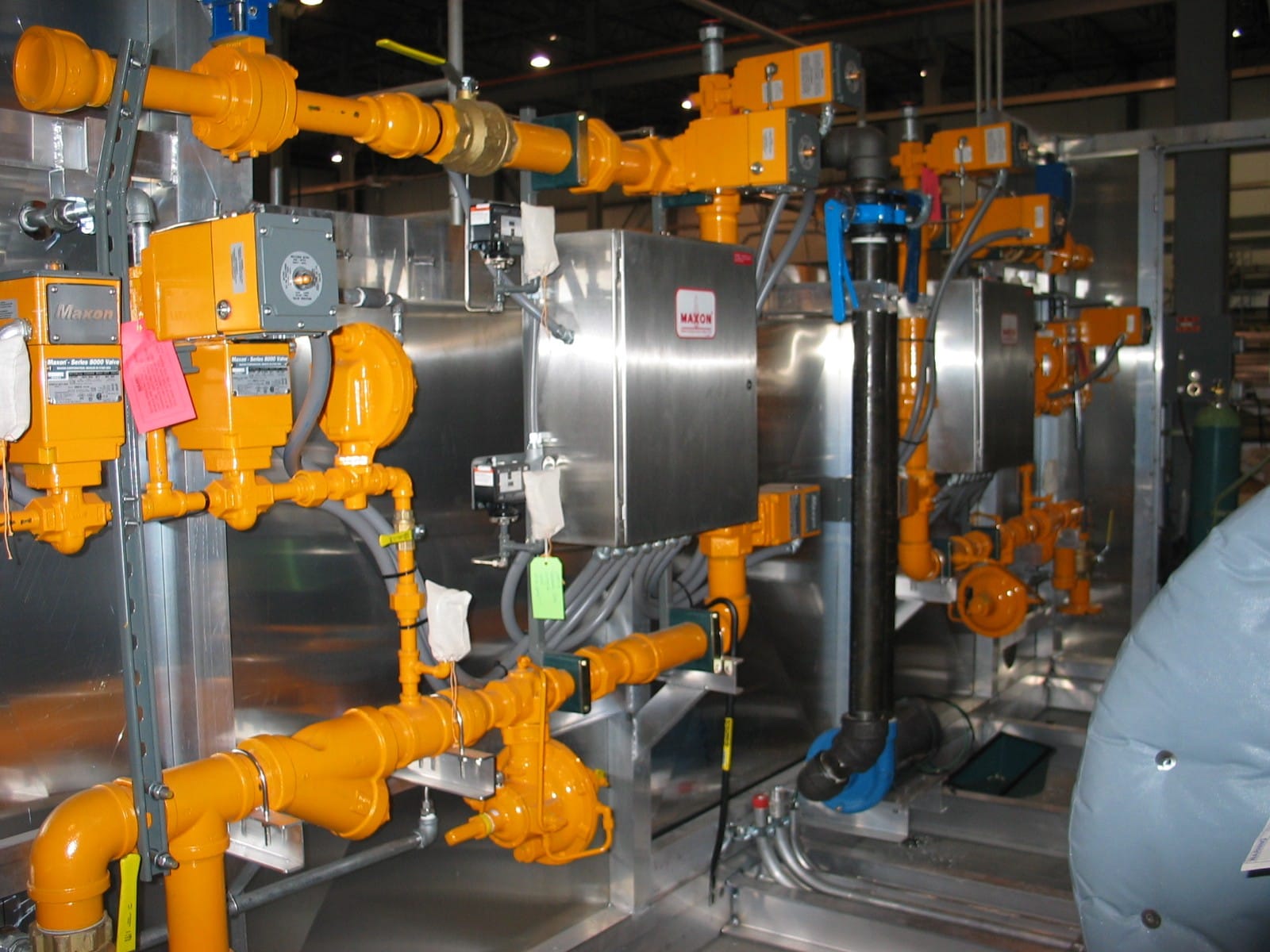 A finished FWM gas-train valve skid with orange process piping, Maxon valves, and stainless control enclosures mounted on an aluminum frame