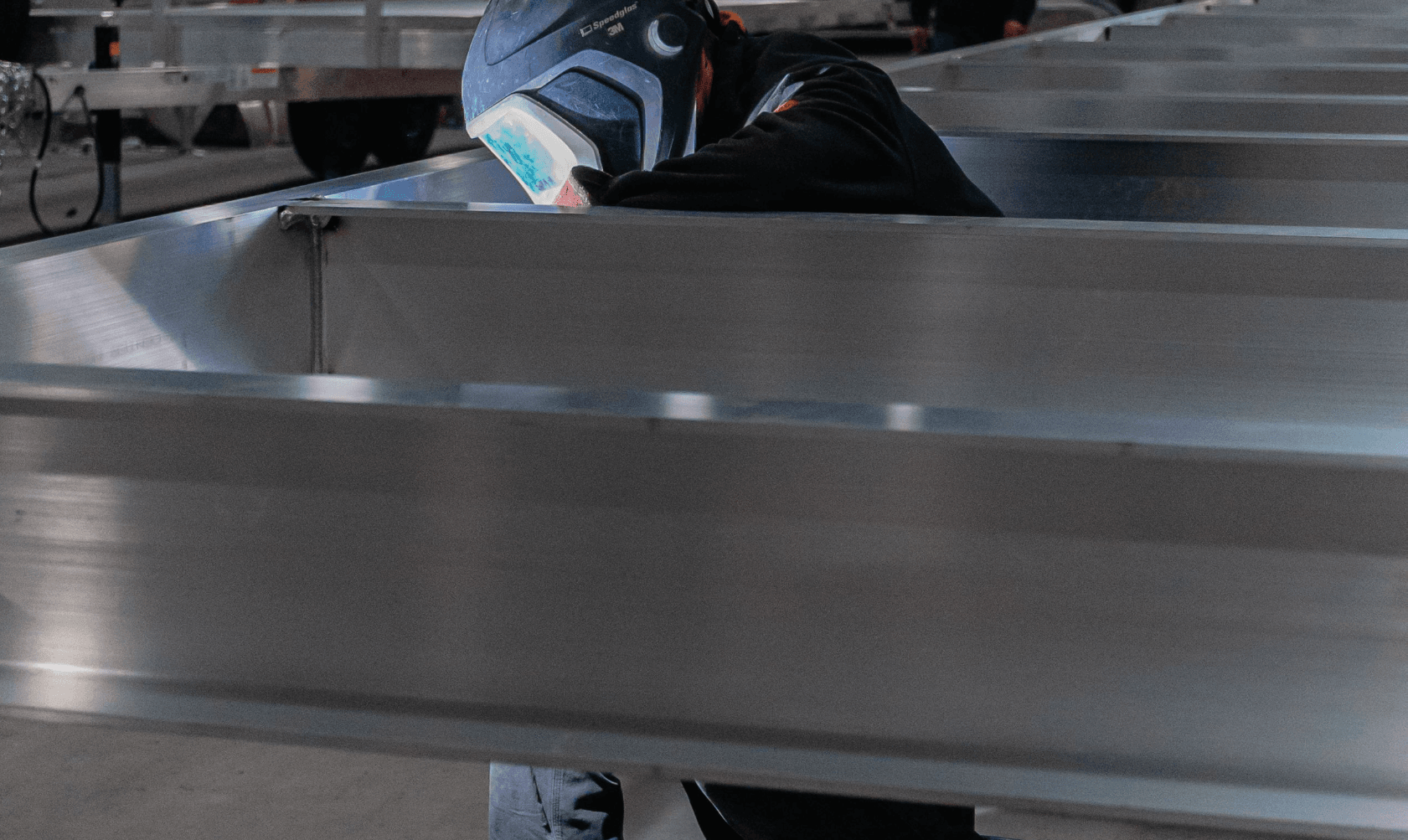 An FWM welder in a 3M Speedglas mask welding a large aluminum frame weldment during domestic production