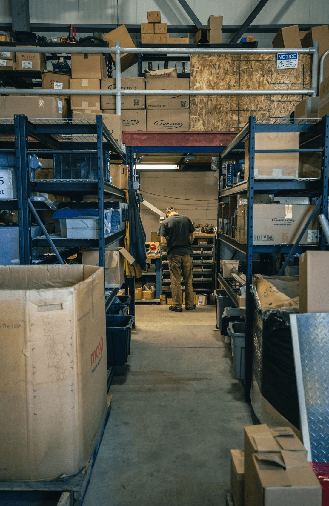 An FWM team member picking components in a stocked parts room with racked inventory and bins