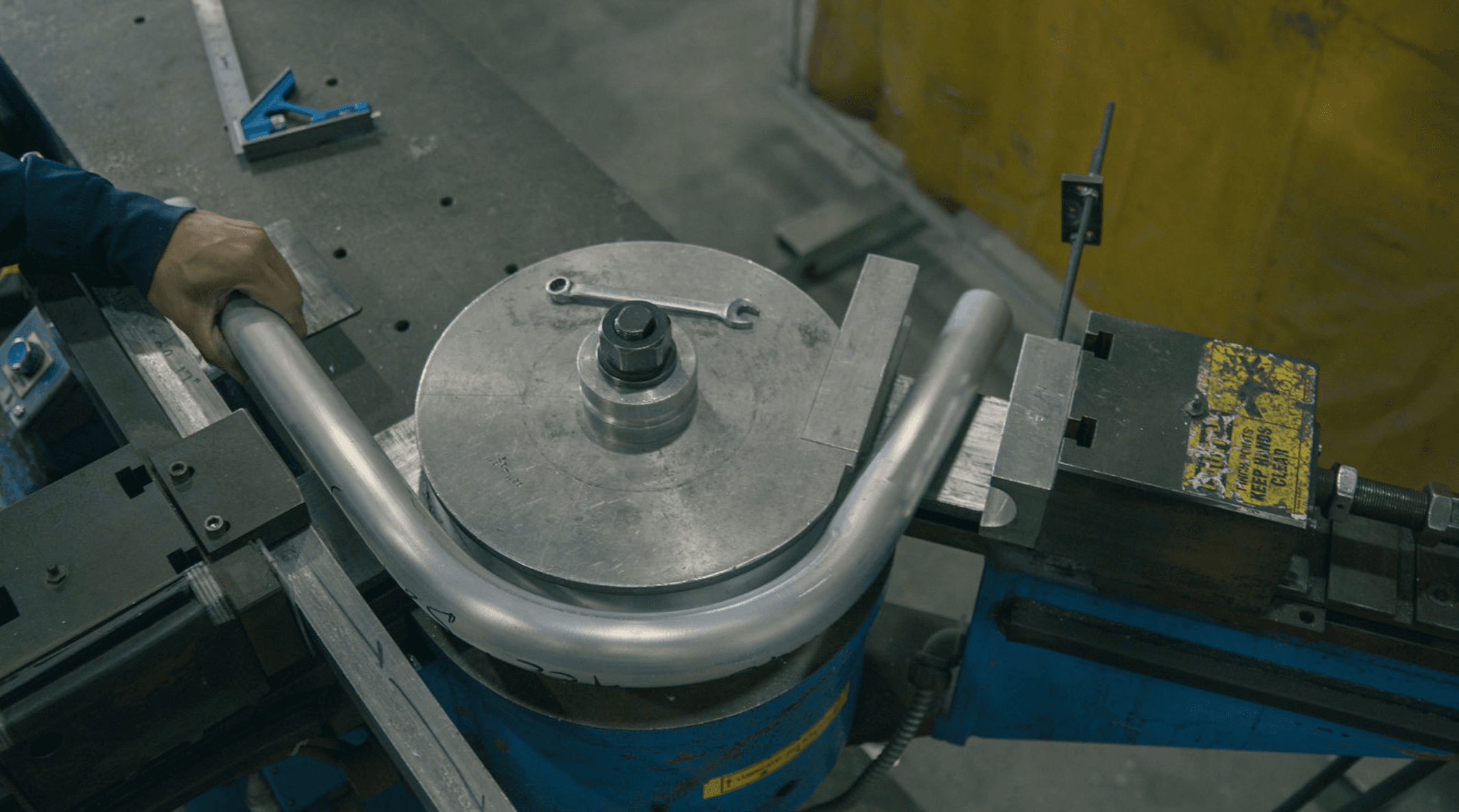 An FWM operator guiding an aluminum tube around a rotary draw bending die on the shop floor