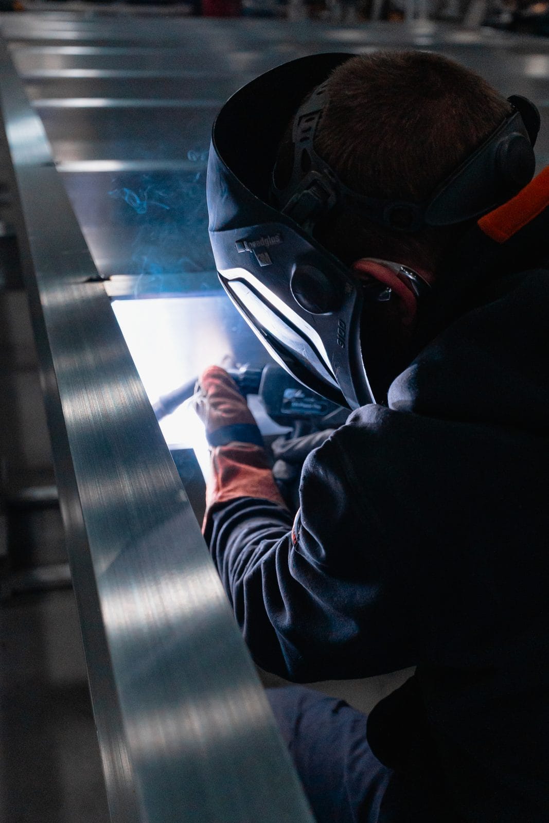 An FWM welder hunched over a long aluminum seam at a welding station
