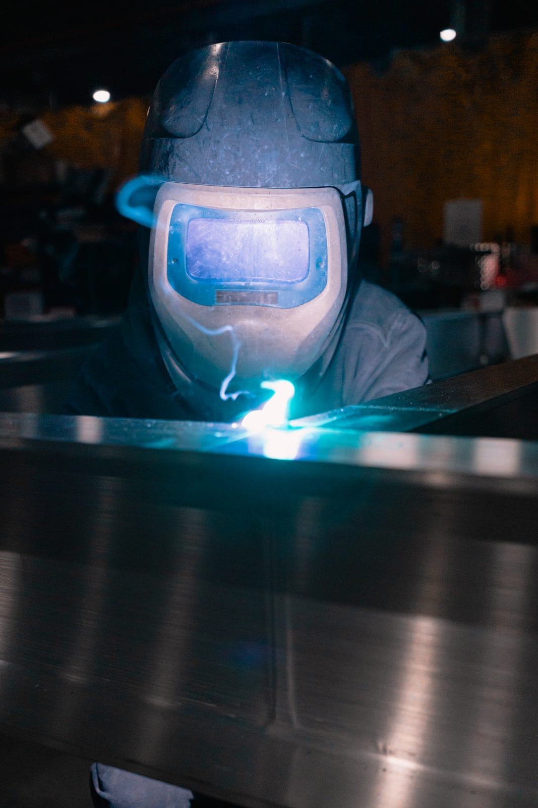 An FWM welder in a helmet welding an aluminum assembly with the weld arc glowing